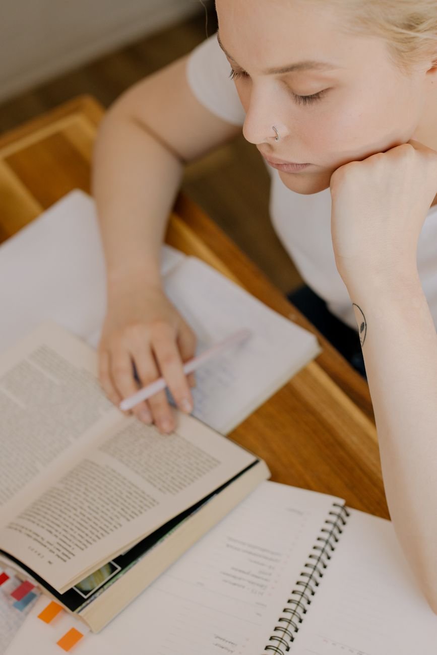 Focused young woman studying with open books and notes at a desk.